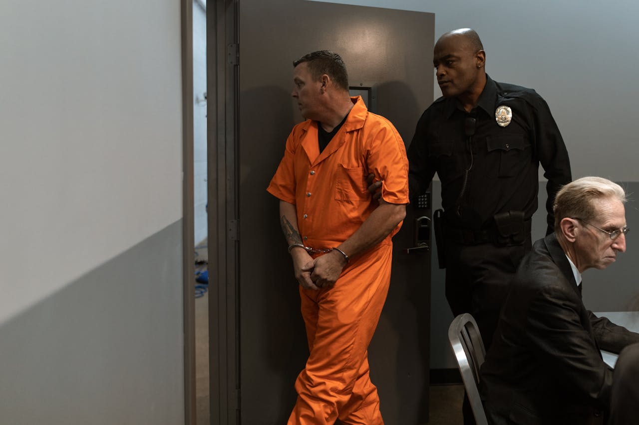 creative-03 Prisoner in orange jumpsuit being escorted by a correctional officer through facility.