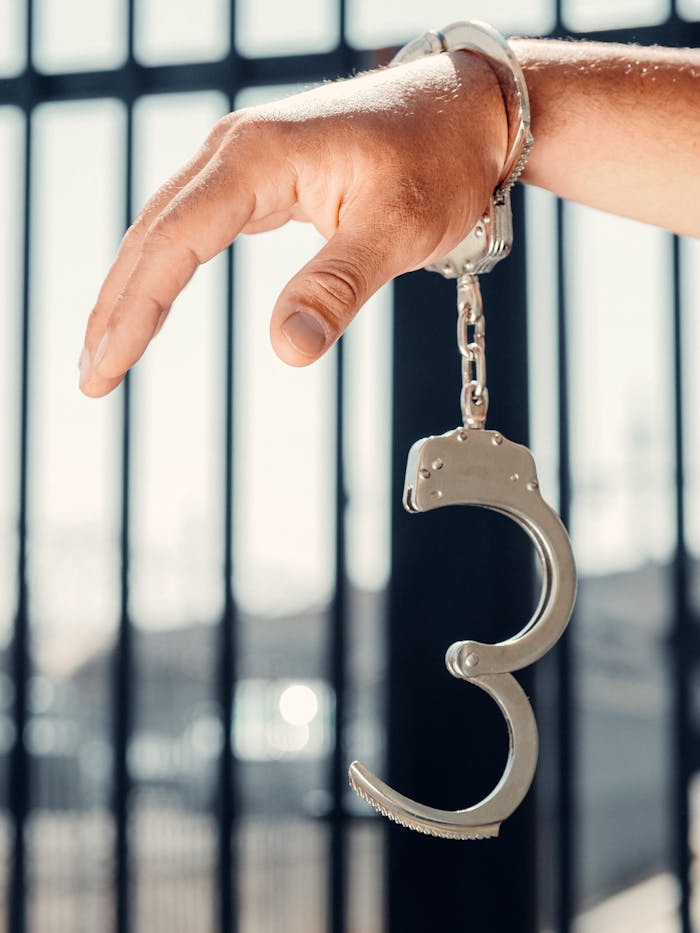 creative-03 Hand grasping open handcuff with prison bars behind, symbolizing crime and justice.